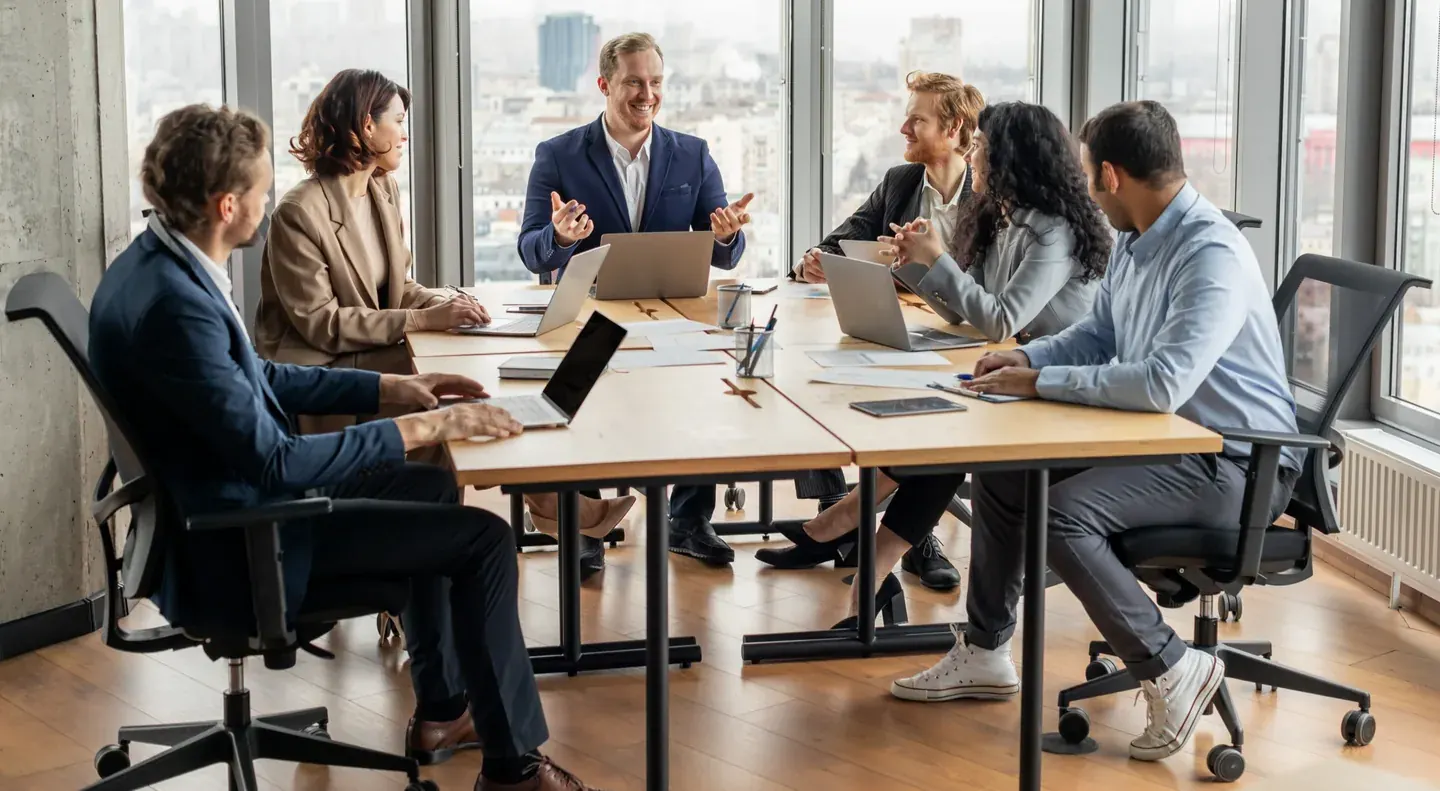 Colleagues in discussion around a meeting table, one gesturing at notes